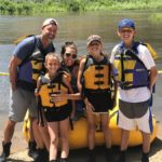 family wearing life jackets posing near water