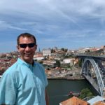 man posing in front of bridge leading to a town